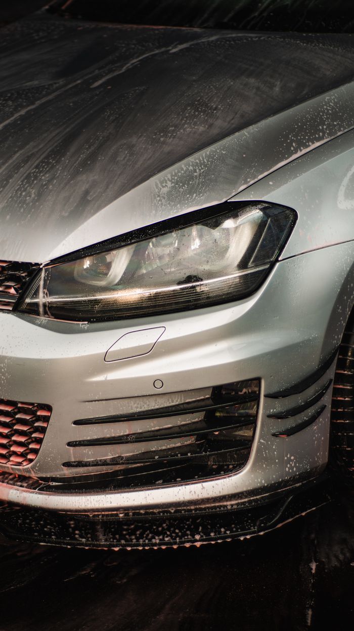 why-choose-us Detailed view of a silver car's front with droplets, highlighting chrome features.