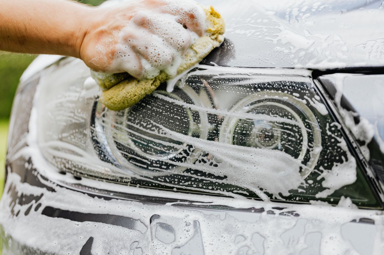 brand-01 Hand scrubbing a car headlight with sponge and soap suds, detailing process.