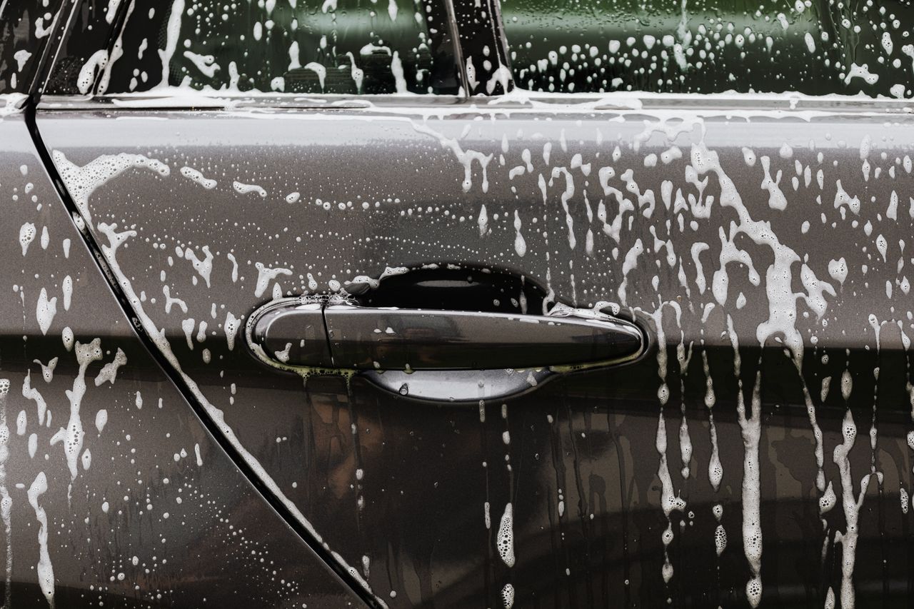 creative-03 Detailed close-up of soap suds on a black car door during a wash, highlighting automotive care.