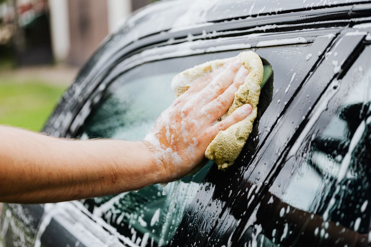 creative A hand scrubs a car window with a sponge, covered in soap suds, during a car wash.