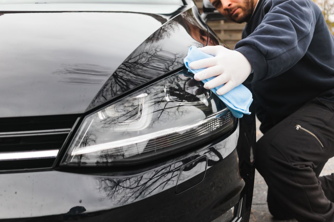 creative-02 Close-up of a man cleaning a car headlight using a blue cloth outdoors.