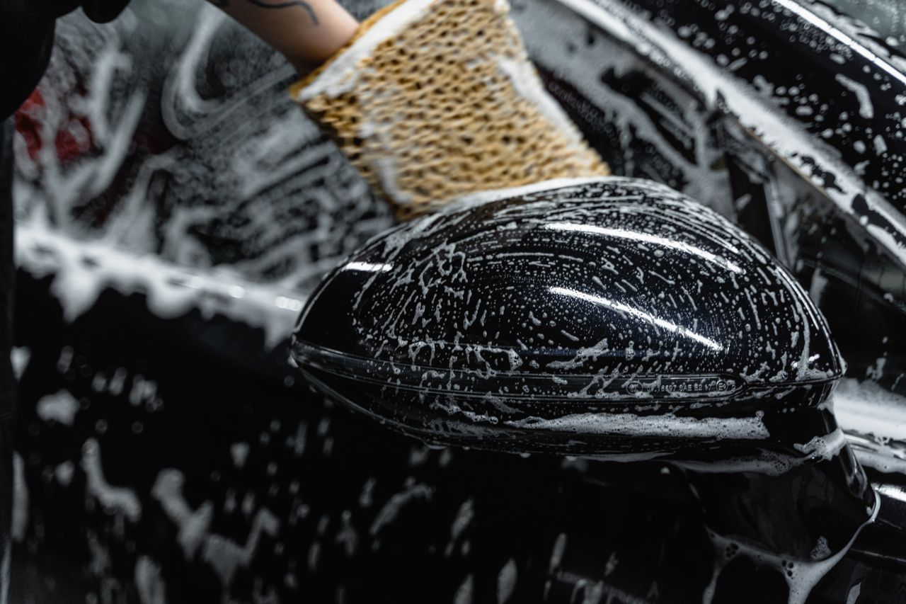 creative-01 Hand scrubbing a car mirror with a sponge covered in soap at a car wash.