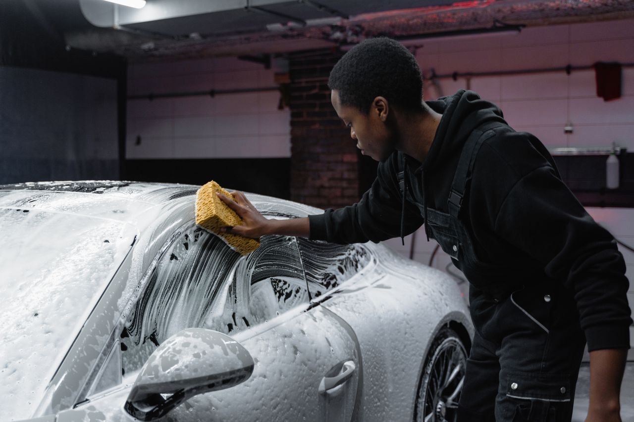 brand-02 A young man cleans a luxury car with a sponge in an indoor carwash setting.