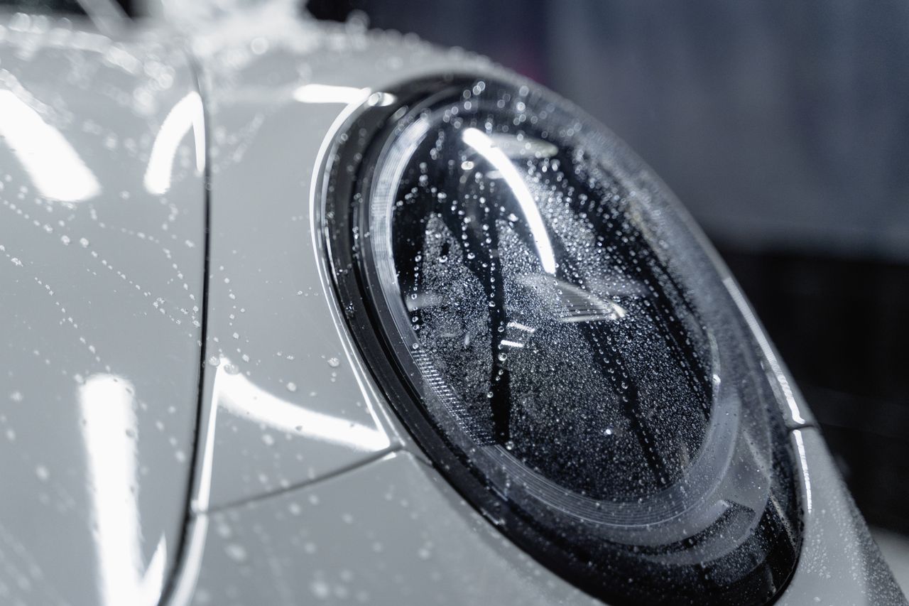 creative-03 A detailed shot of a car headlight covered in water droplets, showcasing automotive design.